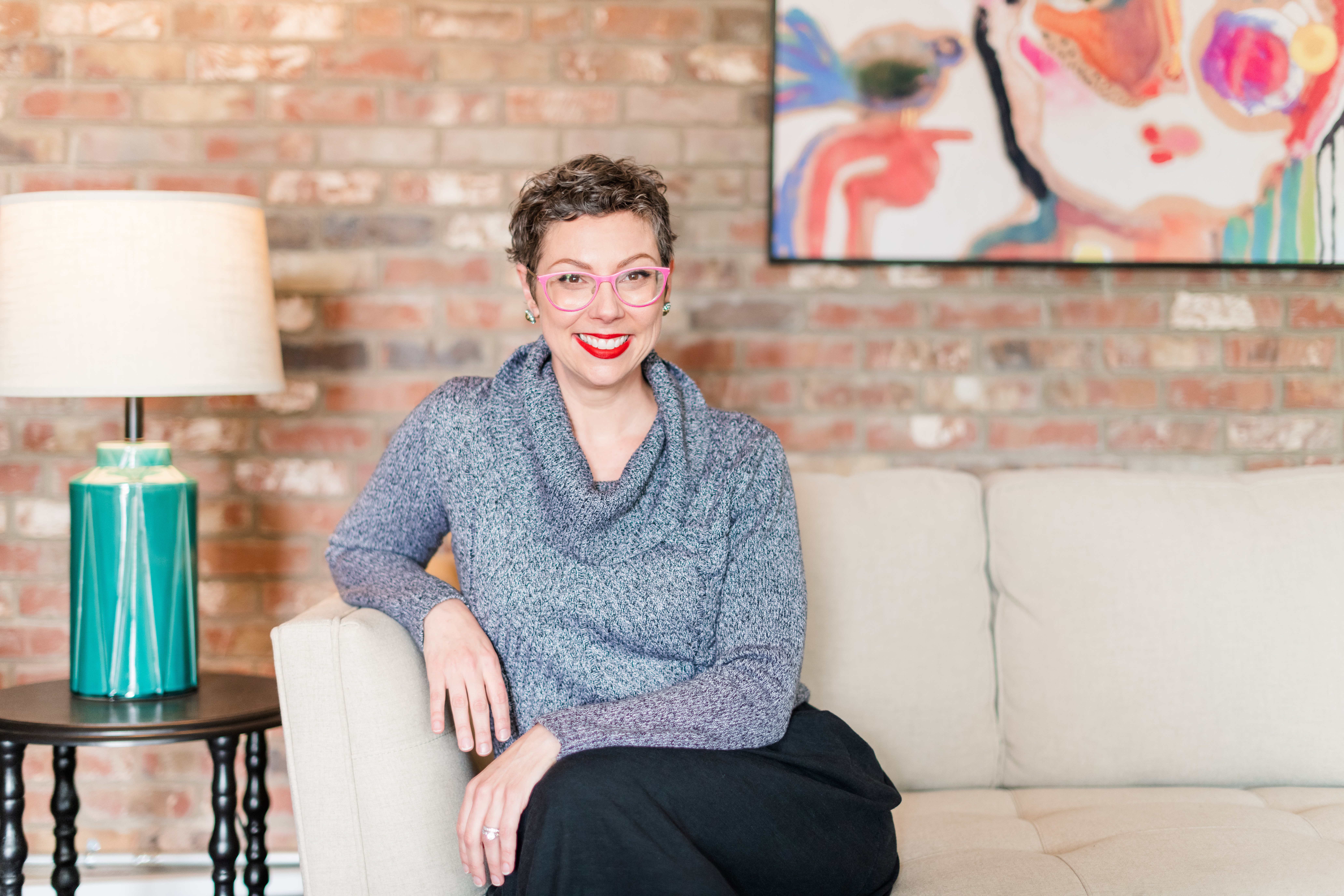 Allison Puryear, LCSW, seated in her therapy office in Asheville NC with exposed brick wall and colorful art