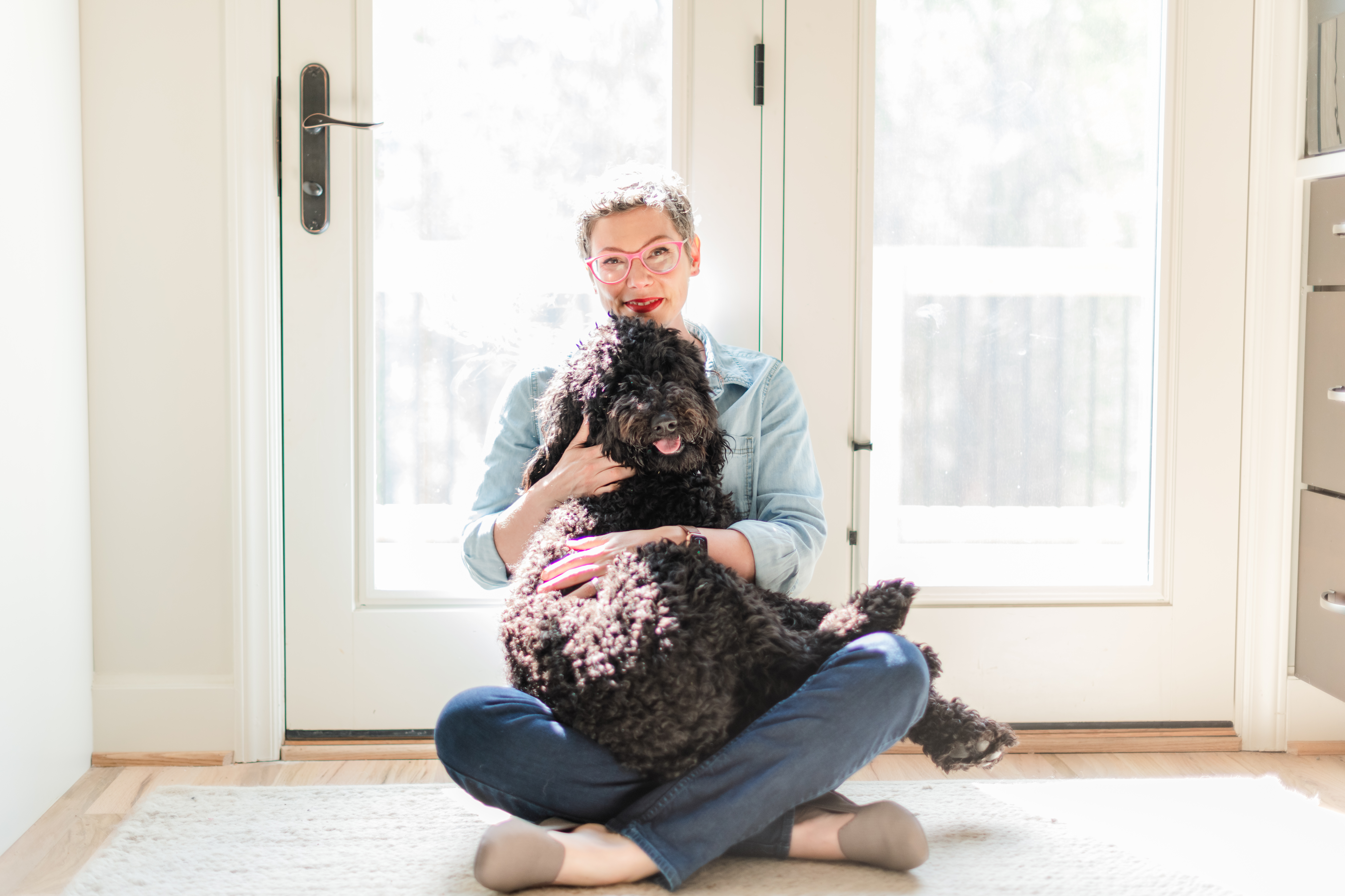 Allison Puryear sitting on the floor at home holding her large black dog in her lap